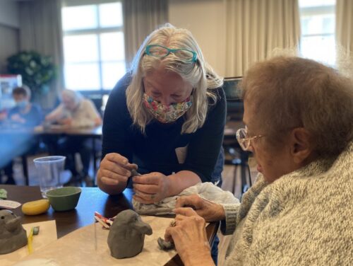 Brenda jones teaching creative aging participant how to make clay bird.