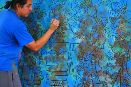 David stands in front a large mural with a paintbrush in one hand 