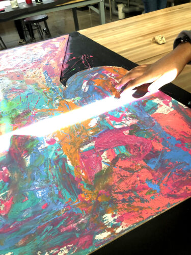 A hand is shown working on an art piece filled with vibrant colors.