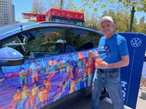 Tony Ortega standing next to the All Electric ID.4 car he brightly painted with faceless figures. 