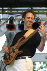 Michael Friedman playing a guitar on stage wearing a black top and white pants